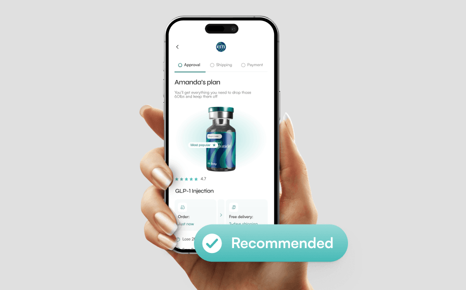 A hand holding a smartphone against a neutral gray background, displaying a mobile health app interface. The screen shows a personalized plan titled Amelia's plan for a GLP-1 injection, featuring a 3D render of a medical vial with a teal and navy logo. Above the phone, a large teal floating button with a white checkmark icon reads Recommended. The UI design is minimalist with teal accents and includes progress indicators for Approval, Shipping, and Payment.